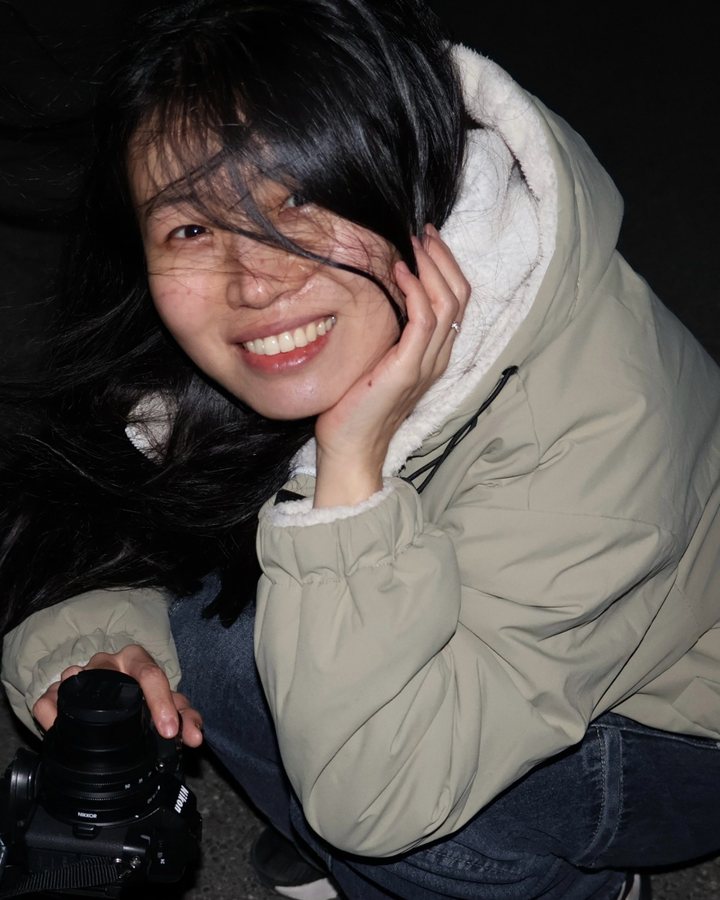 Yunhao Wang crouching at night with a Nikon camera, smiling, hair blown by the wind